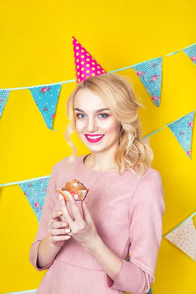 Mulher loira jovem sorridente bonita com um bolo. Celebração e festa.Retrato de estúdio colorido com fundo amarelo — Fotografia de Stock