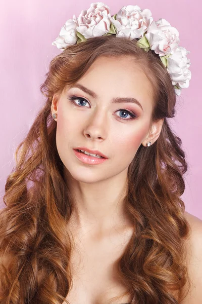 Hermosa joven con un adorno floral en el pelo sobre un fondo rosa — Foto de Stock