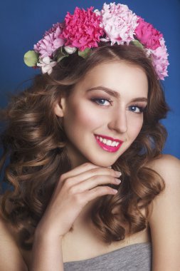 Mavi bir arka plan üzerinde saçında çiçek süsü ile güzel genç kız. Çiçek çelenkli kadın. Güzellik Yüzü. Moda fotoğrafı. Mükemmel makyaj. Cilt bakım konsepti.