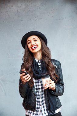 Young pretty girl in hat using smartphone to make a call in the street.