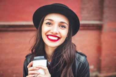 Şapka içkiyle açık trendy kadında. Sokak ve elinde fincan kahve kırmızı dudaklar genç kadınla