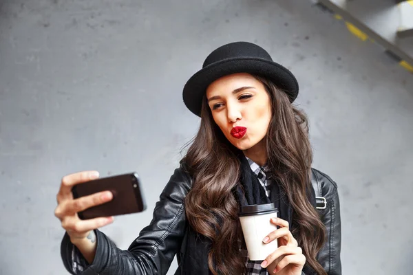 Elég csípő lány vörös ajkak és a kalapban vesz selfie és így kacsa arcát. — Stock Fotó