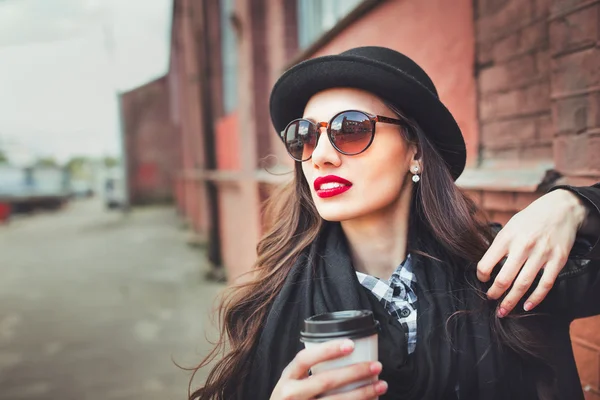 Trendfrau mit Sonnenbrille und Trinkbecher. junge Frau mit Sonnenbrille auf der Straße und einer Tasse Kaffee — Stockfoto
