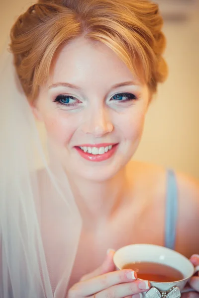 Schöne junge Braut mit Hochzeits-Make-up und Frisur im Schlafzimmer. Morgen der Braut. posiert am Hochzeitsmorgen auf dem Bett. schöne junge Frau in Vernachlässigung in der Früh Tee trinken. — Stockfoto