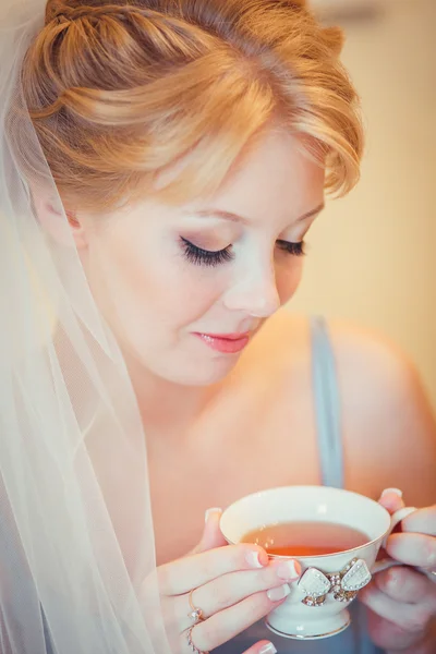 Schöne junge Braut mit Hochzeits-Make-up und Frisur im Schlafzimmer. Morgen der Braut. posiert am Hochzeitsmorgen auf dem Bett. schöne junge Frau in Vernachlässigung in der Früh Tee trinken. — Stockfoto
