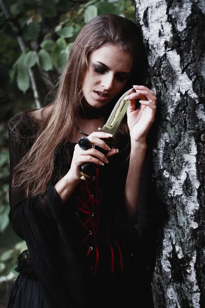 Halloween heks in een donker bos. Mooie jonge vrouw in heksen kostuum. Achtergrond van de horror voor Halloween Concept — Stockfoto