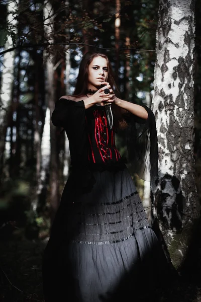 Strega di Halloween in una foresta buia. Bella giovane donna in costume da strega. Sfondo di orrore per il concetto di Halloween — Foto Stock
