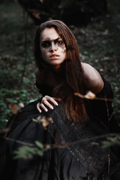 Strega di Halloween in una foresta buia. Bella giovane donna in costume da strega. Sfondo di orrore per il concetto di Halloween — Foto Stock