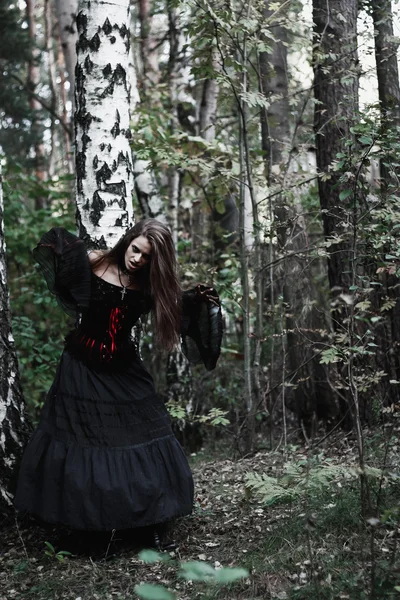 Strega di Halloween in una foresta buia. Bella giovane donna in costume da strega. Sfondo di orrore per il concetto di Halloween — Foto Stock