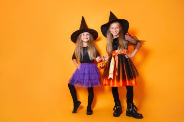 Turuncu arka planda cadı kostümlü mutlu kız çocukları