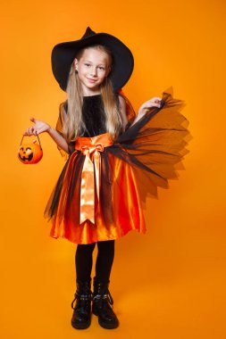 Cadı gibi giyinmiş ve elinde balkabağı sepeti olan küçük bir kız.