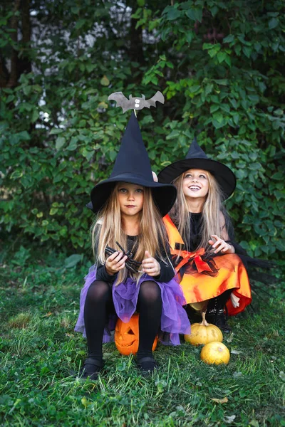Grappige meisjes in heks kostuum voor Halloween zitten op pompoen Jack outdoor — Stockfoto
