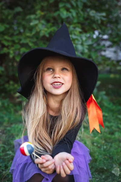 Menina engraçada no traje de bruxa comer doces de Halloween ao ar livre — Fotografia de Stock