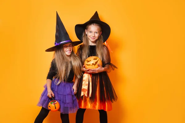 Zwei kleine Mädchen in Halloween-Kostümen amüsieren sich auf orangefarbenem Hintergrund — Stockfoto