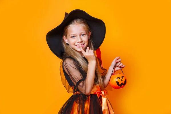 Niña vestida de bruja y sosteniendo una cesta de calabaza sobre fondo naranja — Foto de Stock