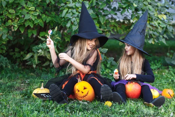 Två roliga små systrar i häxdräkter äter halloween godis — Stockfoto