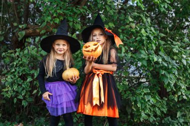 Cadılar Bayramı kostümü giymiş iki çocuk dışarıda şaka mı şeker mi oynuyor.