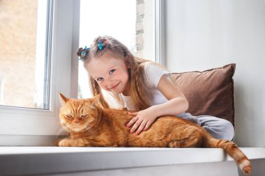 Sevimli çocuk şefkatle kucaklıyor ve penceredeki kırmızı kediyi seviyor.