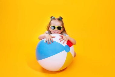 Yaz kızı güneş gözlüğü takıyor, top sarı arka planda gülüyor.