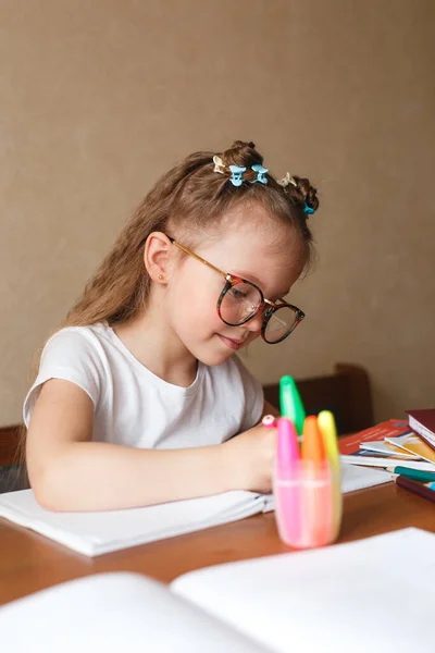Mądra dziewczynka siedząca przy stole, pisząca pracę domową lub przygotowująca się do egzaminu. — Zdjęcie stockowe