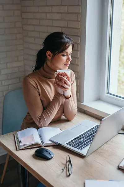 Hermosa mujer joven que trabaja en el ordenador portátil y beber café en casa — Foto de Stock