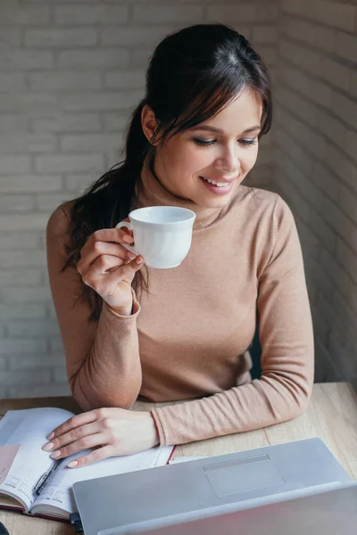 Hermosa mujer joven que trabaja en el ordenador portátil y beber café en casa — Foto de Stock