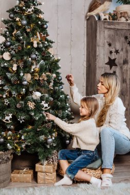 Genç anne ve küçük kızı evde Noel ağacı süslüyorlar.