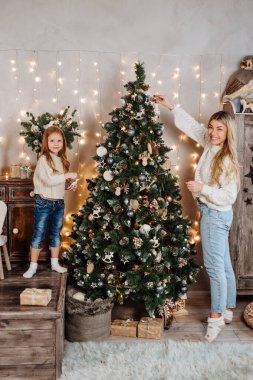 Genç anne ve küçük kızı evde Noel ağacı süslüyorlar.