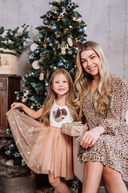 Neşeli anne ve tatlı kızı içeride Noel ağacının yanında oturuyorlar..