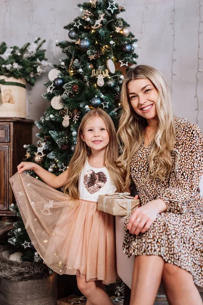 Neşeli anne ve tatlı kızı içeride Noel ağacının yanında oturuyorlar..