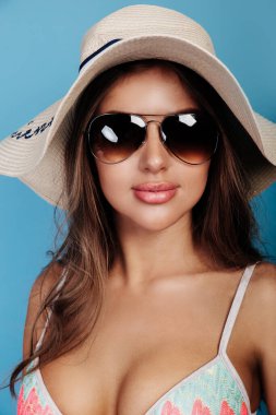 Mavi arka planda güneş gözlüğü ve şapka takan çekici bir kadının yaz portresi.