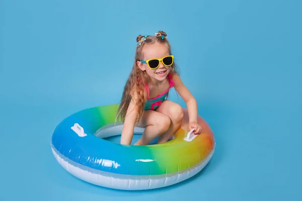 Boldog gyermek lány fürdőruhában és napszemüveg úszás gyűrű kék háttér — Stock Fotó