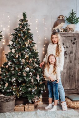 Genç anne ve küçük kızı evde Noel ağacı süslüyorlar.
