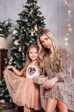 Mutlu Noeller ve mutlu tatiller. Neşeli anne ve tatlı kızı içeride Noel ağacının yanında oturuyorlar..