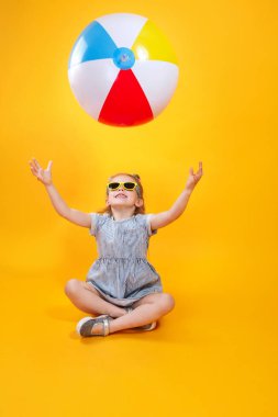 Summer girl wearing sunglasses playing with ball on yellow background