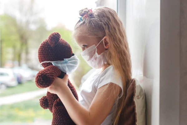Niño y juguete en máscara médica para la protección del virus corona en interiores. Concepto de cuarentena del coronavirus — Foto de Stock