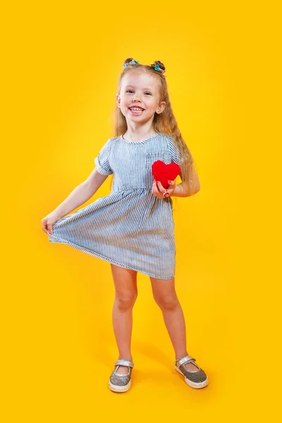노란 배경에 빨간 마음으로 포즈를 취하는 유행하는 드레스를 입은 사랑 스러운 작은 모델 — 스톡 사진