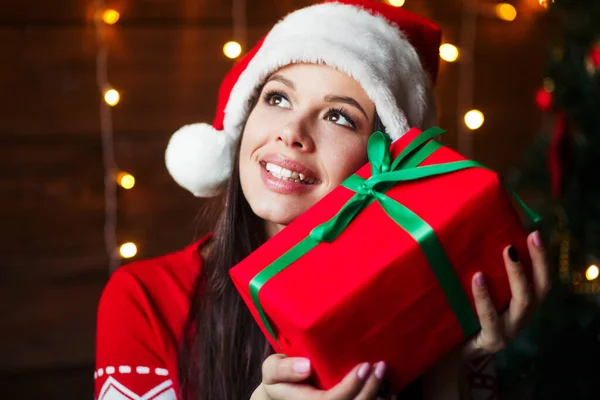 Mujer feliz sosteniendo caja de regalo en las manos usar sombrero de Santa Claus en el fondo de Navidad en casa — Foto de Stock