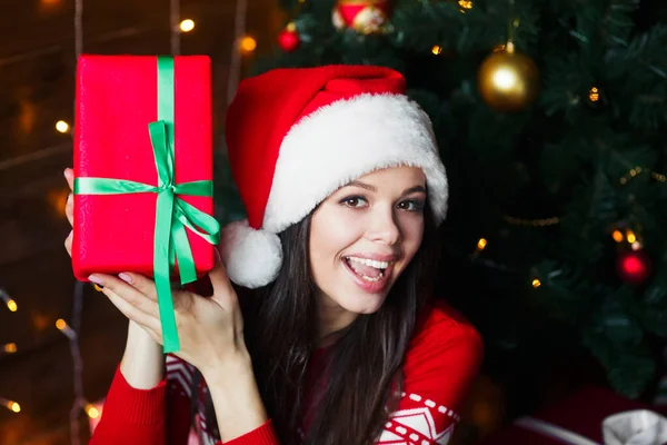 Mujer feliz sosteniendo caja de regalo en las manos usar sombrero de Santa Claus en el fondo de Navidad en casa — Foto de Stock