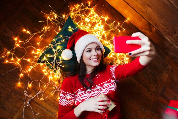 Mujer feliz con sombrero de Navidad tomando una selfie en el fondo de Navidad en casa — Foto de Stock