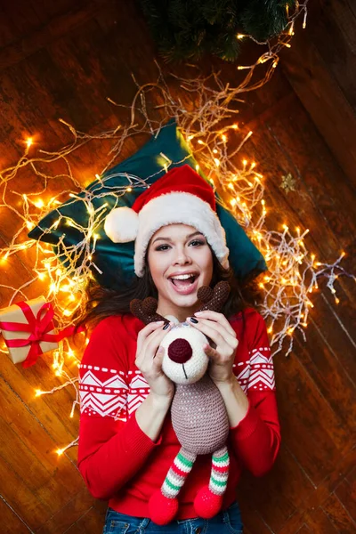 Mujer divertida acostada en el suelo y sosteniendo ciervos presentes en la habitación con decoraciones de Navidad — Foto de Stock