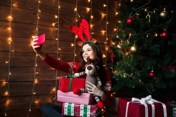 Mujer feliz usando sombrero de Navidad tomando una selfie cerca del árbol de Navidad en casa — Foto de Stock