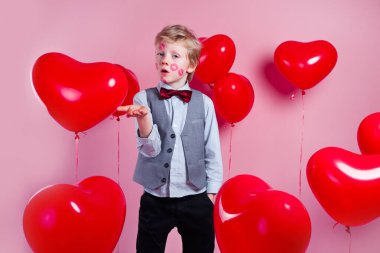 Valentines day. Funny little boy with red kisses on the skin in red balloons in the shape of a heart clipart