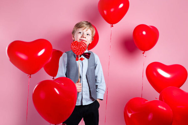 Valentines day. Little cute boy eating candy on red heart balloons background