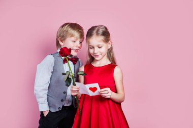 Sevgililer Günü. Elinde sevgililer günü kartı olan altı yaşında tatlı bir kız ve pembe arka planda komik bir çocuk.