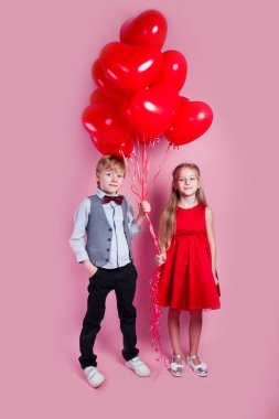 Sevgililer Günü. Pembe arka planda kalp şeklinde balonları olan iki mutlu çocuk. İlk aşk