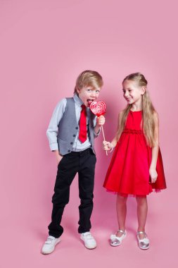 Sevgililer Günü konsepti. Kalp şeklinde şeker kırmızısı lolipopu olan komik çocuk ve küçük kız. Güzel çocuklar tatlı yer..