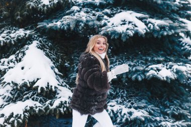 Kürk giymiş gülümseyen kadın kışın karlı ormanda yürüyor..