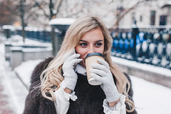 Jovem mulher bebendo café quente e falando ao telefone na cidade fria de inverno — Fotografia de Stock