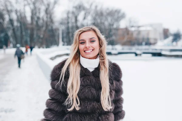 Mulher sorridente vestida em passeios de casaco de pele no inverno parque nevado — Fotografia de Stock